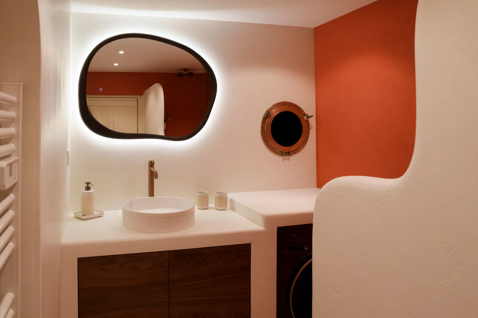 Salle de bain en béton ciré — miroir organique, vasque, mur terracotta — réalisée par DOD&